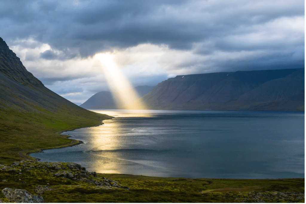 Light shining on body of water near mountains. 