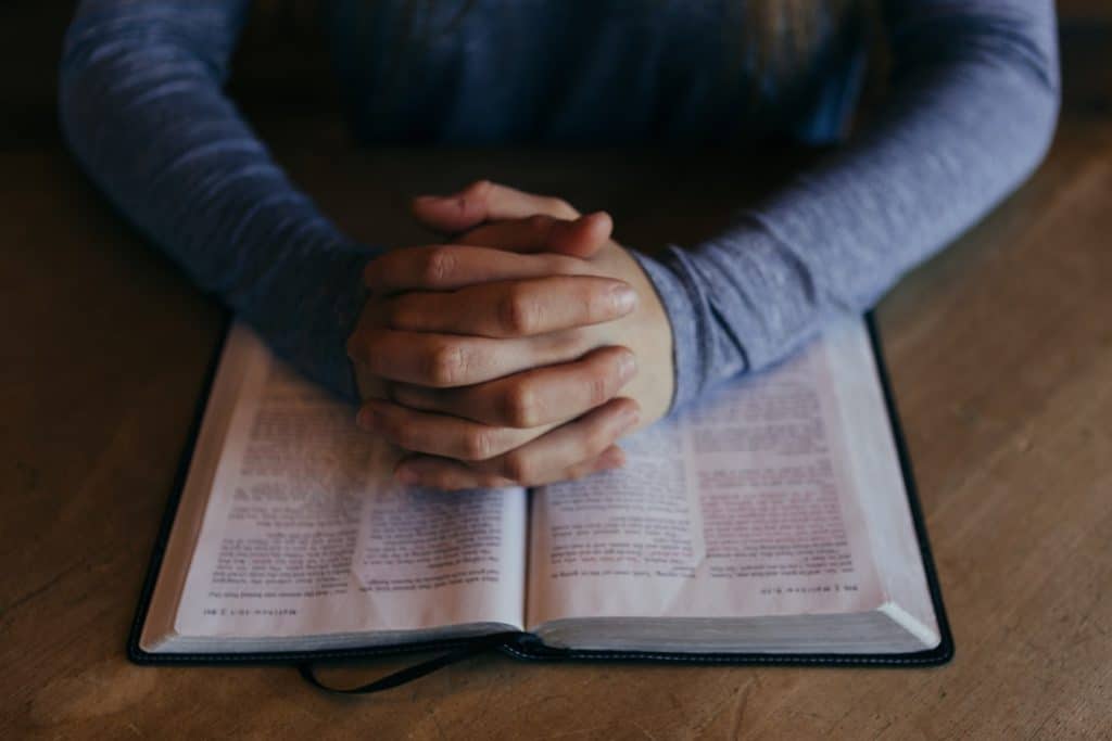 person praying with bible opened on table