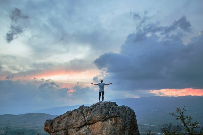 man standing on rock with arms out